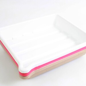 May include: A white rectangular tray with a pink and tan trim. The tray has a simple, clean design, suitable for various uses. The tray is made of a solid material and is set against a white background.