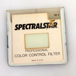 May include: A white plastic case with a clear plastic window showing a yellow filter. The case has the text "SPECTRALSTAR PROFESSIONAL COLOR CONTROL FILTER MADE IN U.S.A." printed on it.