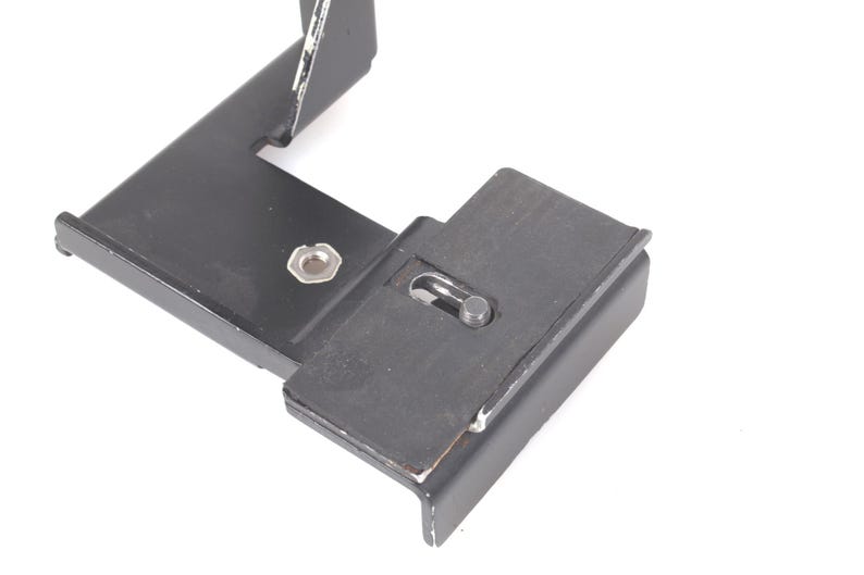 Op de afbeelding: Een zwarte metalen beugel met een rechthoekige basis en een L-vormige arm. De beugel heeft een rubberen pad en een schroef voor bevestiging. Het item is waarschijnlijk een camera-accessoire of montagecomponent.