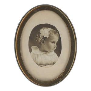 Könnte beinhalten: Ovale antike Fotografie in einem goldfarbenen Rahmen. Das Schwarz-Weiß-Bild zeigt ein junges Kind mit einer Schleife im Haar. Der Rahmen hat einen dunklen Rand und einen hellen Innenraum.