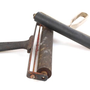 May include: Two vintage paint rollers, one with a black handle and a metal frame, and the other with a silver handle and a black rubber roller.