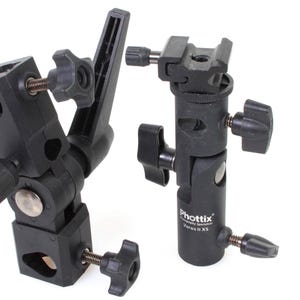 Op de afbeelding: Twee zwarte flitsbeugeladapters. Eén is een draaibare beugel met een vergrendelingsknop en de andere is een verticale beugel met een vergrendelingsknop en de tekst "Phottix V-Hold XS".