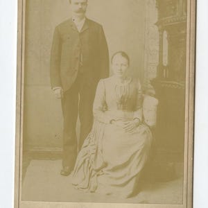 May include: Sepia-toned portrait of a man and a woman. The man stands, wearing a dark suit and a mustache. The woman sits in a chair, wearing a long dress. The photograph is framed with the text "Lothrop & Cunningham" and "489 Westminster St. Providence."