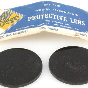May include: Two black, circular protective lenses with a blue and white paper package. The package reads "PROTECTIVE LENS" and "OKI SUPPLY CO." The lenses are 50mm in size.