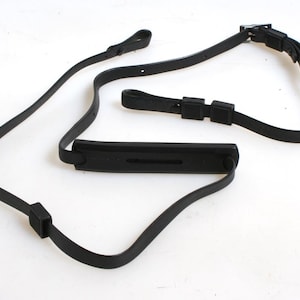 May include: Black leather camera strap with a padded shoulder rest and adjustable length.