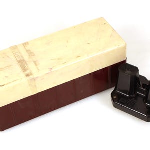 Könnte beinhalten: Vintage schwarzer Stereobetrachter mit einer cremefarbenen und braunen Box. Der Betrachter hat zwei Okulare und eine rechteckige Basis. Die Box ist rechteckig mit einem cremefarbenen Deckel und einem braunen Boden. Die Box hat ein abgenutztes Aussehen.