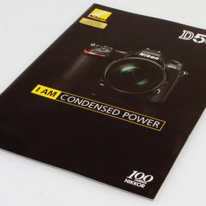May include: A black Nikon D500 camera brochure featuring a yellow Nikon logo at the top, the text D500 in white, and the phrase I AM CONDENSED POWER in a yellow box. The bottom includes the text 100 million NIKKOR in white on a black background.