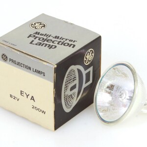 May include: A GE Multi-Mirror Projection Lamp with its original box. The box is beige and black with the GE logo and the words "Projection Lamps" and "EYA 82V 200W". The lamp is silver and has a clear lens.