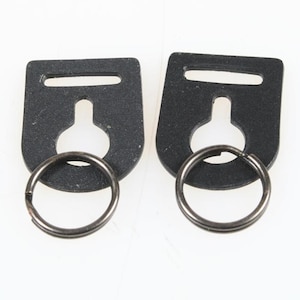 May include: Two black rectangular key fob hardware pieces with a key ring attached. The hardware has a slot at the top and a keyhole shape in the center. The key rings are silver.