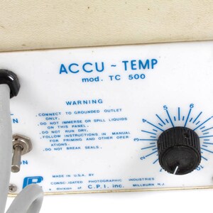 Pu&ograve; includere: Un pannello di controllo bianco con il testo "ACCU-TEMP mod. TC 500" e un'etichetta di avvertenza. Il pannello ha una manopola nera con un quadrante che va da 2 a 9. Il testo sull'etichetta recita: "CONNECT TO GROUNDED OUTLET ONLY. DO NOT IMMERSE OR SPILL LIQUIDS ON THIS PANEL. DO NOT RUN DRY. FOLLOW INSTRUCTIONS IN MANUAL FOR PRIMING AND OTHER OPERATIONS. DO NOT BREAK SEALS."