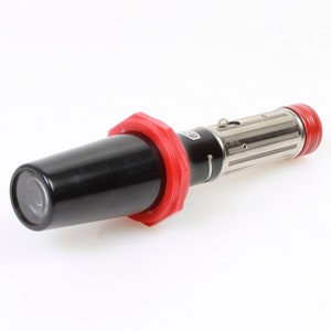 Puede incluir: Una linterna de plata y negro con un anillo rojo alrededor de la lente. La linterna tiene un cuerpo acanalado y una cubierta de lente de plástico negro.