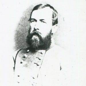 May include: A black and white historical portrait of a person with a full beard and short hair, wearing a military-style jacket featuring a double row of buttons on the chest. The image has a grainy, aged texture with visible light exposure.
