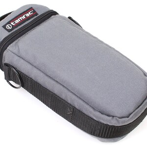 May include: Gray camera lens case with a black zipper and a black strap with a metal ring. The case has the word "tamrac" printed on the front.