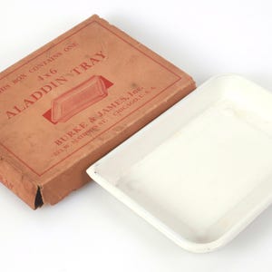 May include: A rectangular white tray next to its original brown cardboard box. The box is printed with the text: THIS BOX CONTAINS ONE 4x6 ALADDIN TRAY, BURKE & JAMES, INC., 321 W. MADISON ST., CHICAGO, U.S.A. The tray has a smooth, shallow basin.