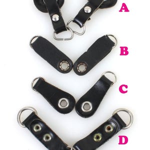 以下が含まれることがあります： 金属製のリングとハトメが付いた、黒色の革製のストラップループが4種類あります。ループにはA、B、C、Dのラベルが付いています。