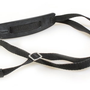 May include: Black camera strap with a padded neck strap and adjustable length. The strap has a silver metal buckle and the word "Canon" printed on the neck strap.