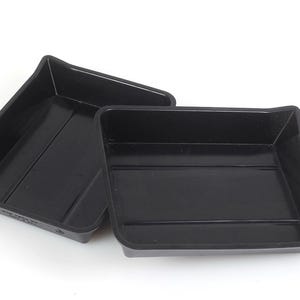 May include: Two rectangular black plastic trays with raised edges and a smooth interior surface. Each tray features a slightly angled side wall and a flat base, designed for holding small items or organizing supplies in a workspace or storage area.