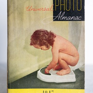 May include: A vintage book cover for the "Universal Photo Almanac" from 1947. The cover features a black and white photo of a young child standing on a scale, with the title "Universal Photo Almanac" in red and yellow lettering.