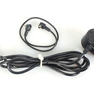 May include: A black electrical cord with a black plug on one end and a black connector with the text "AC ADAPTER" on the other end. The cord is coiled and there are two additional black cords with plugs on each end.