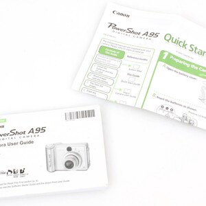 May include: Two instruction manuals for a Canon PowerShot A95 digital camera. The camera user guide is white with a black and white image of the camera. The quick start guide is white with green text and a black and white illustration of the camera.