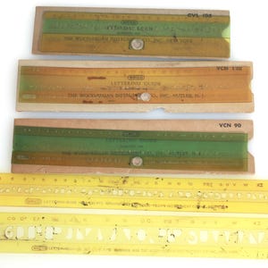 May include: A selection of vintage lettering guides and stencils. The guides have green, brown, and yellow hues with printed text. The stencils are yellow with letter cutouts. The items are from The Wood-Regan Instrument Co.