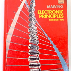 May include: A hardcover textbook titled Electronic Principles Third Edition by Malvino with a bright red cover. The front features a graphic of numerous silver cylindrical electronic components arranged in a curved line with thin metal leads extending outward.