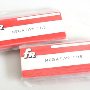 Puede incluir: Dos cajas de almacenamiento de plástico rojo y blanco con el texto "fr NEGATIVE FILE" impreso en la parte delantera. Las cajas están envueltas en plástico transparente.