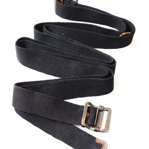 May include: Black canvas belt with a metal buckle and loop. The belt is made of a woven fabric and has a rectangular buckle with a toothed edge. The belt is shown against a white background.