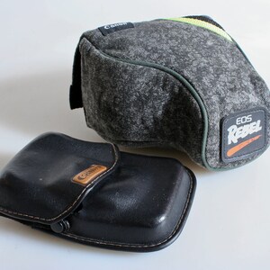 May include: Two camera cases, one grey with the text "EOS Rebel" and the other black with the text "Canon".