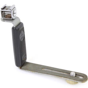 Puede incluir: Un soporte de flash para cámara negro y plateado con un agarre texturizado. El soporte tiene una placa de metal con un tornillo en el extremo.