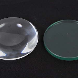 Puede incluir: Dos lentes de vidrio redondas, una transparente y otra verde, sobre un fondo negro.