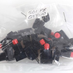 Può includere: Un sacchetto di plastica trasparente pieno di interruttori a pulsante neri con coperchi rossi. L'etichetta dice "501 PB QTY-10". Gli interruttori sono probabilmente per elettronica o uso industriale.