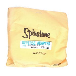 Puede incluir: Una bolsa de papel amarilla con el texto "Spiratone Reverse Adapter for Minolta 7000 49mm W/F.Stop Japan" impreso en ella.