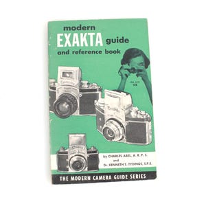 Puede incluir: Un libro verde vintage titulado "modern EXAKTA guide and reference book" con ilustraciones de cámaras. La portada presenta a una mujer tomando una foto y el texto "THE MODERN CAMERA GUIDE SERIES".