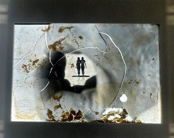 Könnte beinhalten: Beschädigtes, rechteckiges Bild mit einer Silhouette von zwei nebeneinander stehenden Figuren. Das Bild ist in einem Rahmen eingefasst, mit Rissen und Verfärbungen auf der Oberfläche. Die Figuren befinden sich in einem hellen Bereich, umgeben von einem dunklen, verschwommenen Hintergrund.