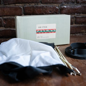 Könnte beinhalten: Ein Fotografie-Softbox-Kit mit einer Box mit der Aufschrift "BRITEK". Das Kit enthält eine weiße und schwarze Softbox, einen schwarzen Montage-Ring und mehrere Stützstangen. Die Box hat ein gestreiftes Muster.