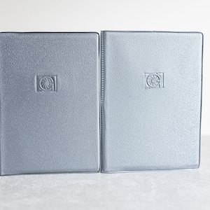 May include: Two silver-colored photo albums with a raised, circular logo on the front cover.