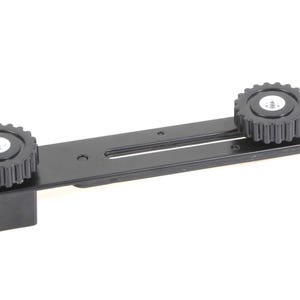 May include: Black metal camera accessory with two adjustable knobs. The accessory has a slot for sliding a camera or other equipment.