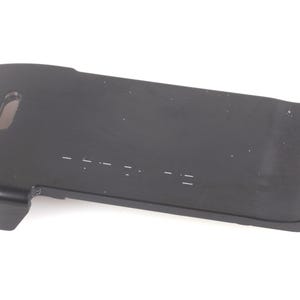 May include: A black, rectangular plastic battery pack with a smooth, matte finish. The unit features a rounded edge on one side, a small rectangular cutout near the top, and a series of faint, horizontal white markings along the center surface.