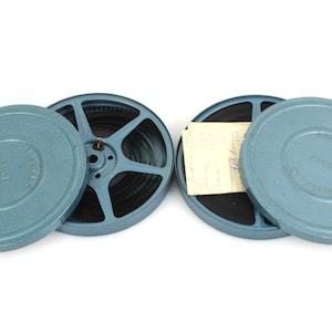 Puede incluir: Dos latas de película de metal azul con las tapas abiertas, revelando un rollo de película y un trozo de papel dentro de una de las latas.