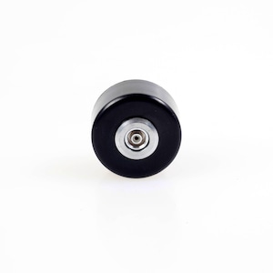 May include: A black cylindrical object with a silver-colored center, likely a bottle stopper or similar item. The object is centered on a white background, showcasing its simple, modern design. The stopper's smooth, dark surface contrasts with the metallic detail.