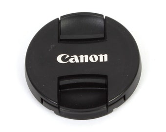 May include: A black Canon lens cap with a clip on the side.