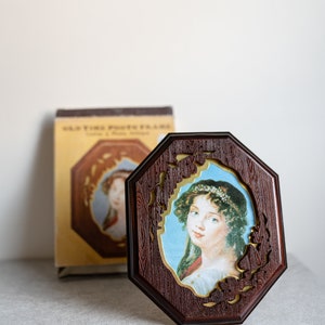 May include: A wooden octagonal picture frame with a gold trim and a floral design. The frame features a portrait of a woman with a white headband and a white dress.