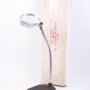 May include: A vintage magnifying glass with a flexible chrome neck and a black base. The round lens is held in a chrome frame. The product is in its original packaging, which includes the text "TESTRITE INSTRUMENT CO., INC."
