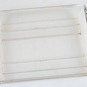 May include: A clear, rectangular acrylic tray with rounded corners. The tray has four horizontal dividers, creating five sections. The transparent design allows for visibility of contents. Ideal for organizing small items.