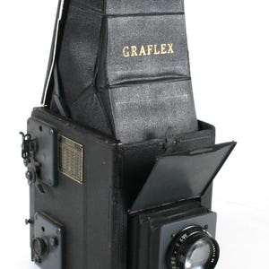 Könnte beinhalten: Eine schwarze Vintage-Graflex-Kamera mit Balg und Objektiv. Die Kamera hat eine Lederverkleidung und ein Metallgehäuse.