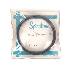 May include: A Spiratone Proxi Far Model 10 lens filter, 62 mm, in its original packaging. The packaging is clear plastic with a white and blue label. The text "MADE IN JAPAN" is visible.