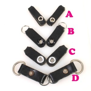 以下が含まれることがあります： 金属製のリングが付いた黒い革製のストラップループが4つ。ループはサイズが異なり、黒または銀のアイレットが付いています。ループにはA、B、C、Dのラベルが付いています。