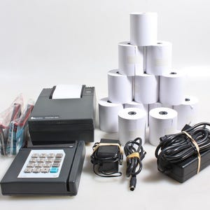 May include: A selection of point-of-sale equipment, including a black printer, a keypad, rolls of white paper, and a power adapter. The printer has a sheet of paper emerging from it. There are also ink cartridges and cables.
