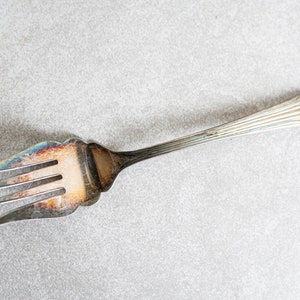 May include: A silver fork with a decorative handle. The fork has four tines and is slightly tarnished.